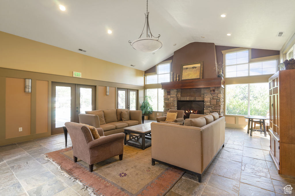 Living area with stone tile flooring, a fireplace, recessed lighting, high vaulted ceiling, and french doors