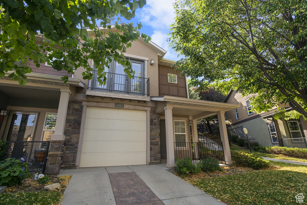 View of front of home featuring stone siding, a balcony, a garage, driveway, and covered porch