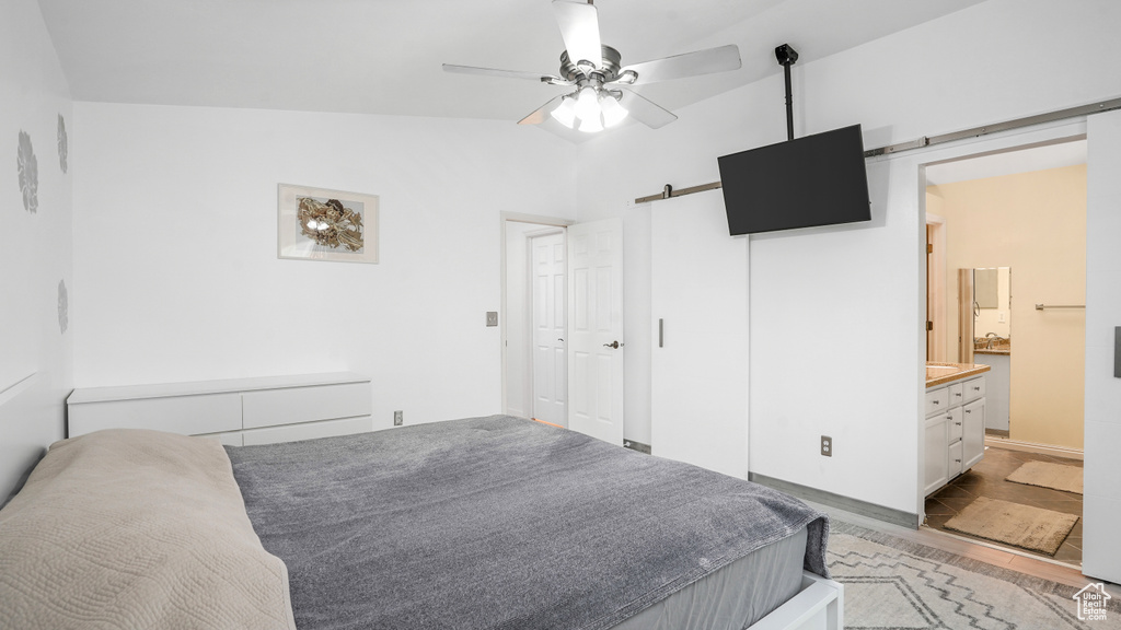 Bedroom featuring a barn door, light wood finished floors, vaulted ceiling, a ceiling fan, and ensuite bath