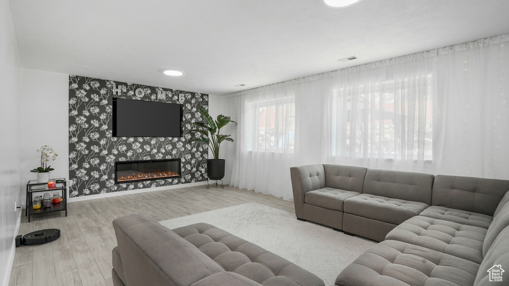 Living room with wood finished floors, a fireplace, an accent wall, and wallpapered walls
