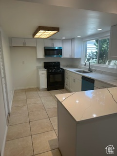 Kitchen with black appliances, light stone countertops, light tile patterned flooring, a peninsula, and white cabinets
