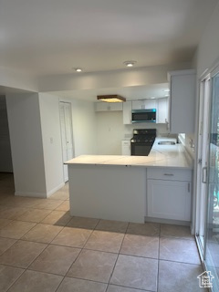 Kitchen featuring stove, stainless steel microwave, a peninsula, light countertops, and light tile patterned floors