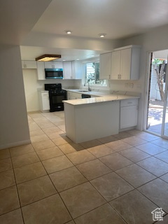 Kitchen with black gas range, a peninsula, light tile patterned floors, light countertops, and white cabinetry