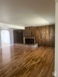 Unfurnished living room with a fireplace, wood finished floors, wooden walls, and arched walkways
