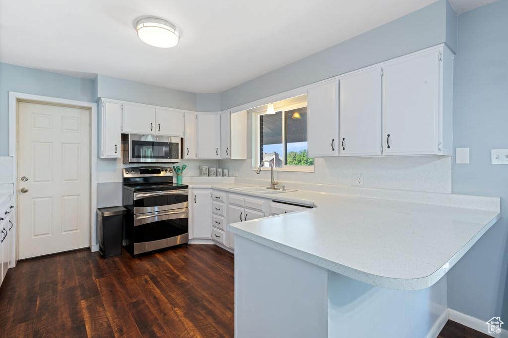 Kitchen with appliances with stainless steel finishes, dark wood-type flooring, a peninsula, and light countertops