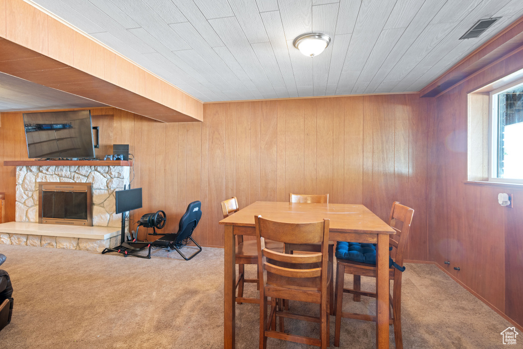 Carpeted dining area featuring wooden walls and a stone fireplace