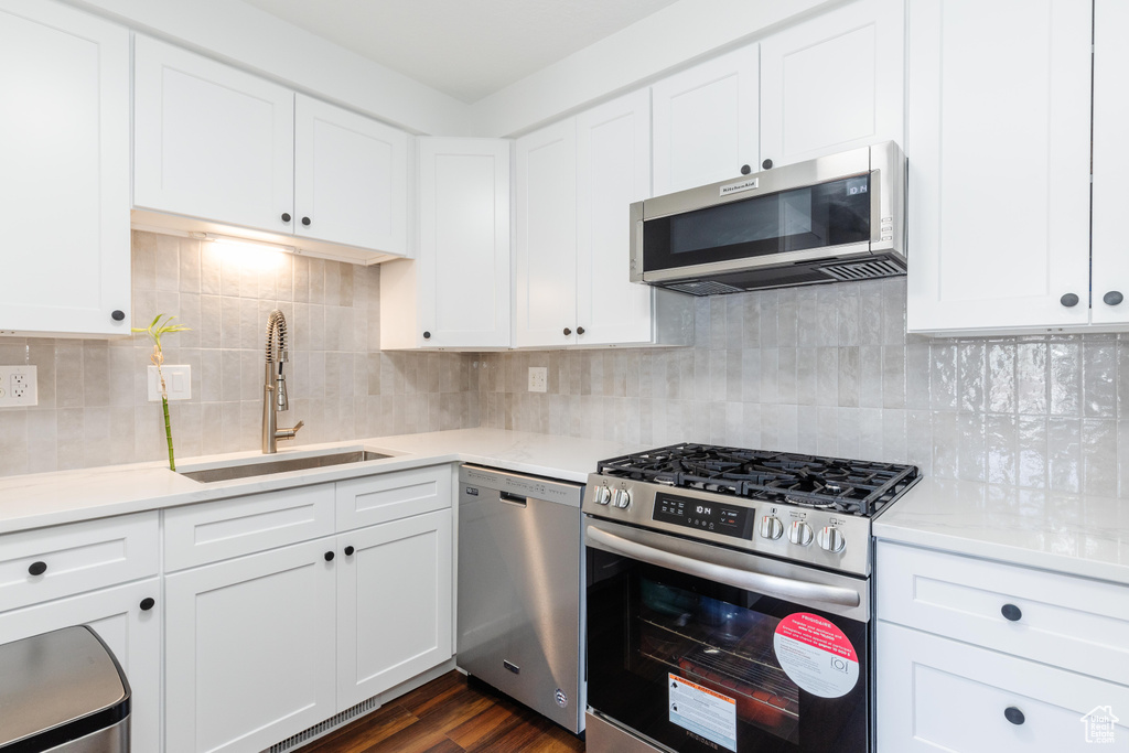 Kitchen featuring stainless steel appliances, light countertops, white cabinetry, and dark wood finished floors