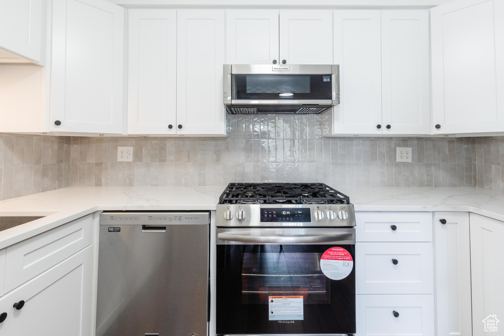 Kitchen featuring stainless steel appliances, white cabinetry, decorative backsplash, and light stone counters