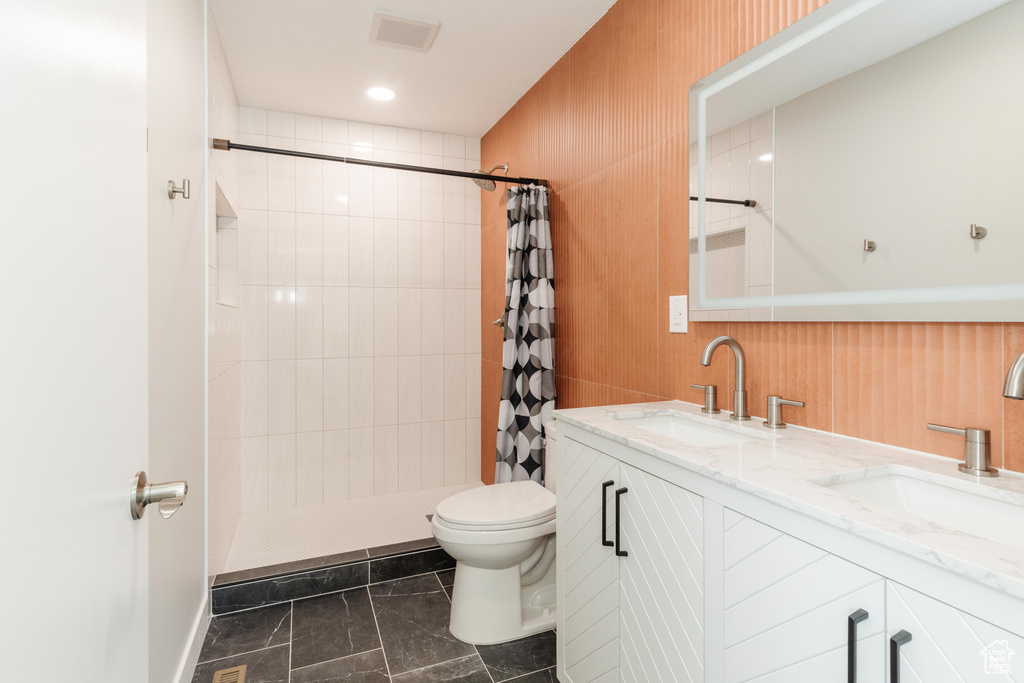 Bathroom with a tile shower, double vanity, and marble finish flooring