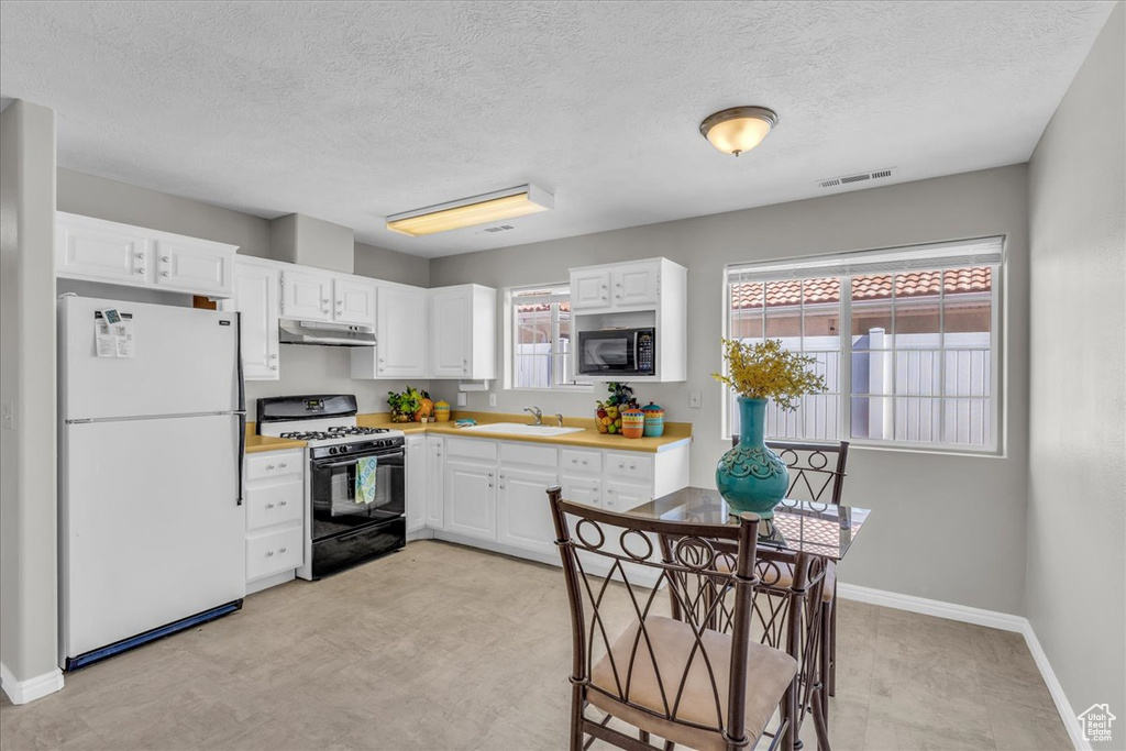 Kitchen with freestanding refrigerator, gas range oven, black microwave, white cabinets, and under cabinet range hood