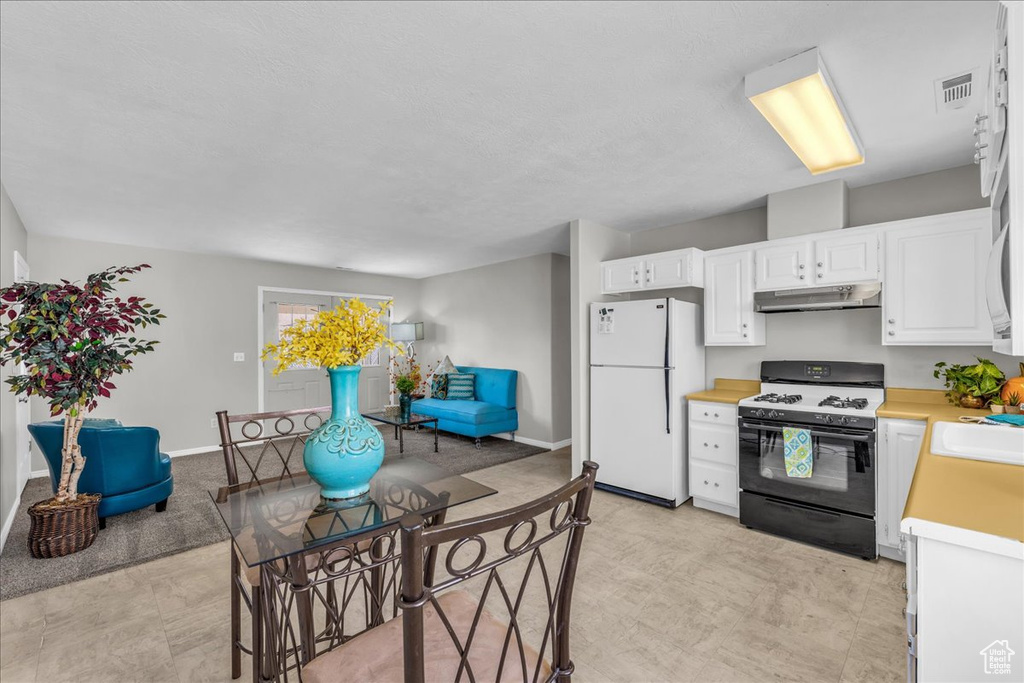 Kitchen with gas stove, freestanding refrigerator, under cabinet range hood, light countertops, and white cabinetry