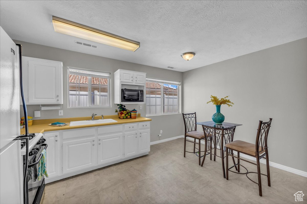 Kitchen with gas range oven, black microwave, light countertops, white cabinets, and a textured ceiling