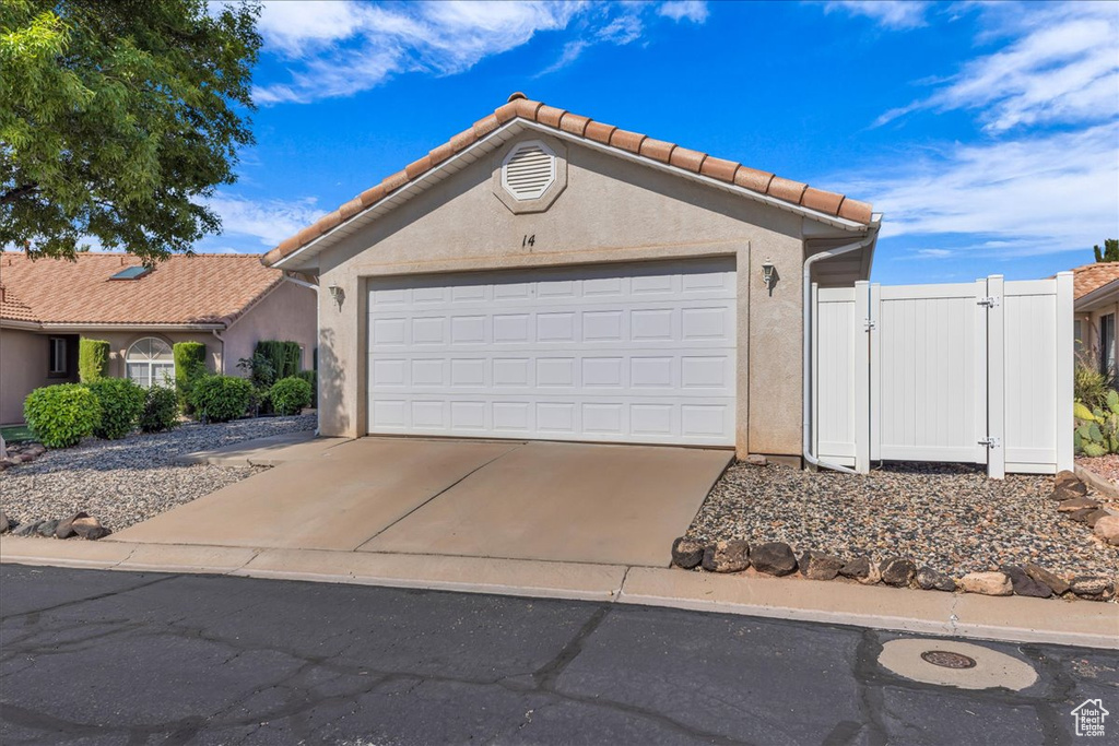 View of front of property featuring stucco siding, a gate, a garage, driveway, and a tiled roof