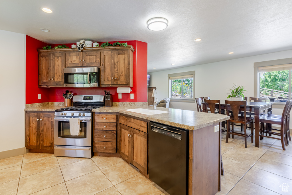 Kitchen featuring appliances with stainless steel finishes, a peninsula, recessed lighting, brown cabinets, and light countertops