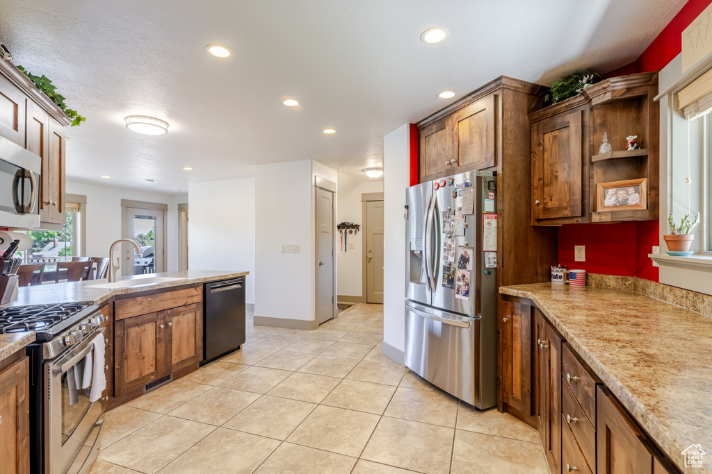 Kitchen featuring appliances with stainless steel finishes, recessed lighting, light tile patterned floors, open shelves, and brown cabinetry