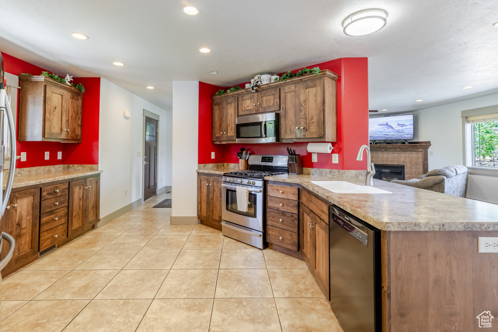Kitchen with appliances with stainless steel finishes, recessed lighting, light tile patterned flooring, a glass covered fireplace, and light countertops