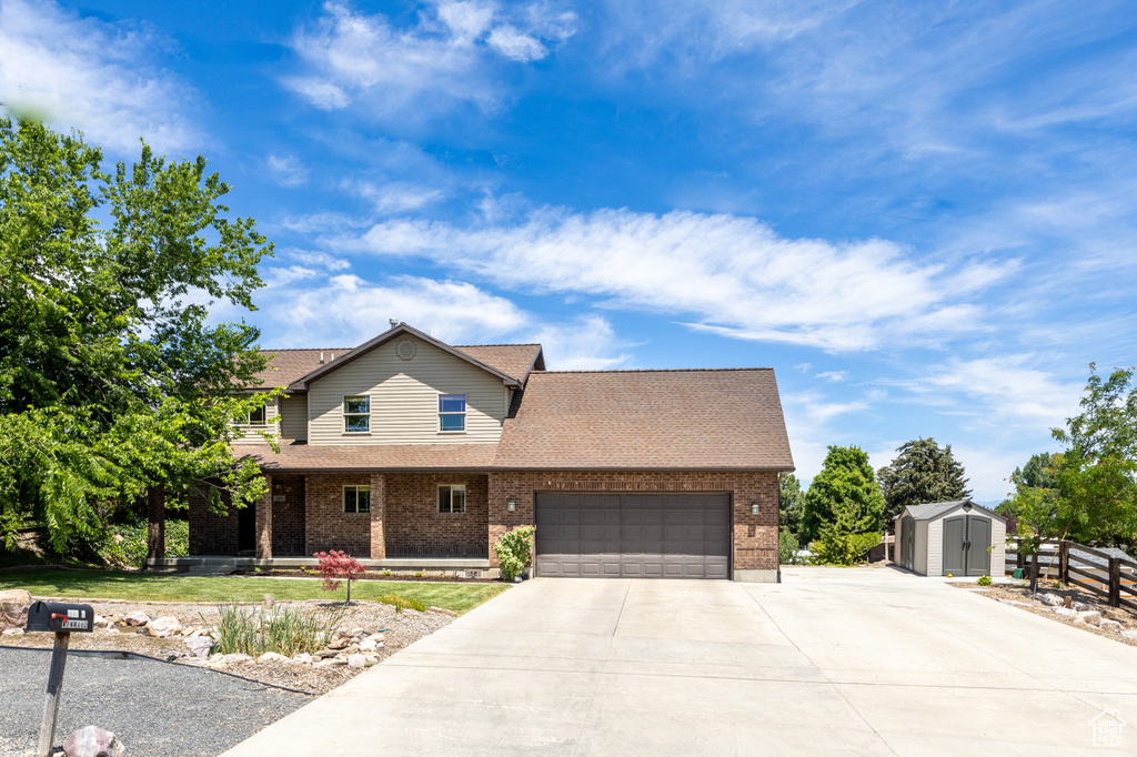 View of front of property with driveway, a storage unit, an attached garage, brick siding, and covered porch