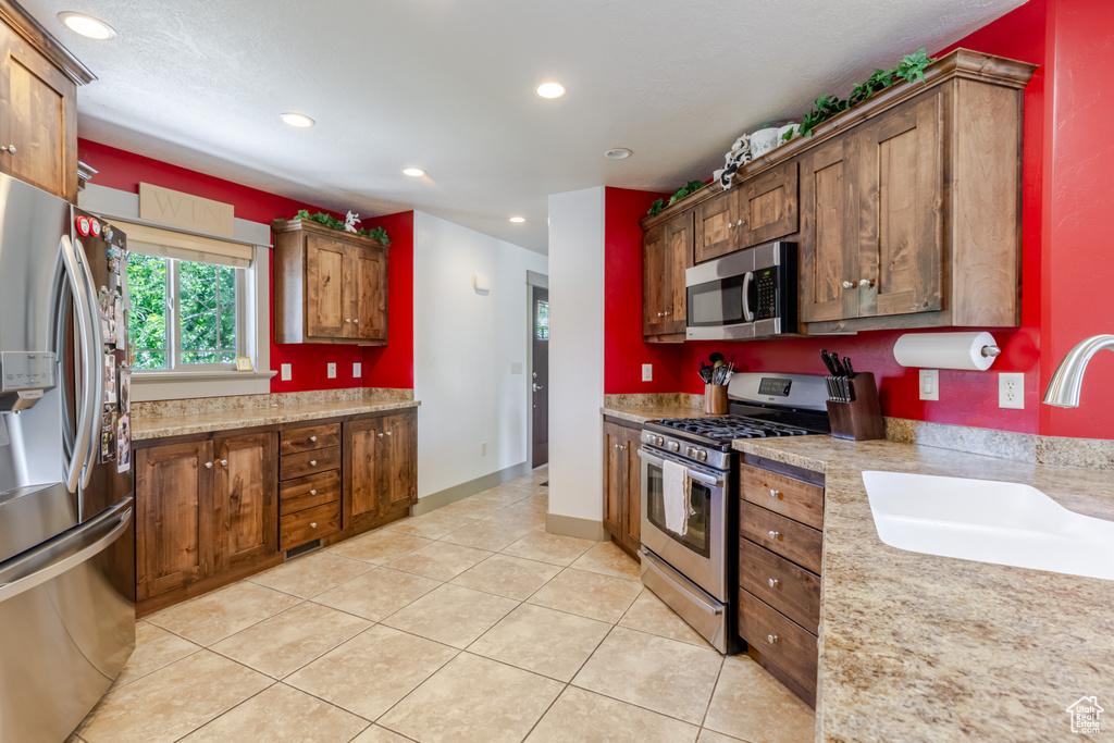 Kitchen with appliances with stainless steel finishes, light tile patterned floors, recessed lighting, and brown cabinets