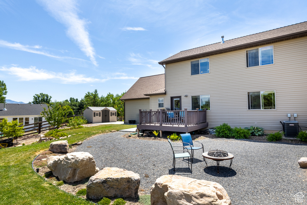 Rear view of property with a fire pit, a storage unit, a wooden deck, a patio area, and roof with shingles