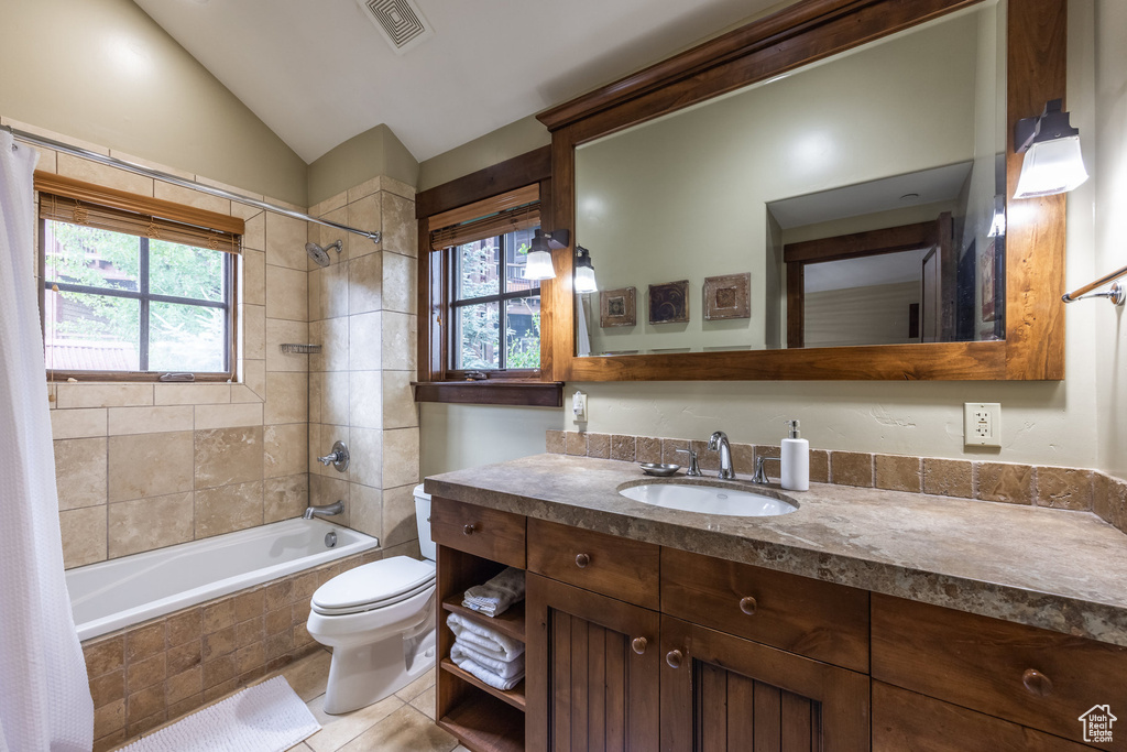 Bathroom with tiled shower / bath combo, vanity, plenty of natural light, lofted ceiling, and tile patterned floors