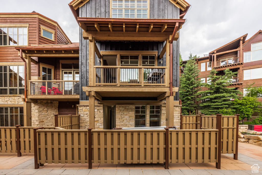 Rear view of house with a balcony, stone siding, and board and batten siding