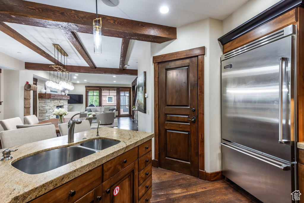 Kitchen featuring stainless steel built in fridge, dark wood finished floors, beamed ceiling, light stone countertops, and hanging light fixtures