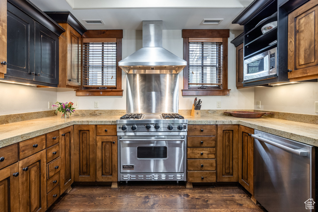 Kitchen featuring appliances with stainless steel finishes, wall chimney range hood, dark wood-style floors, and light countertops