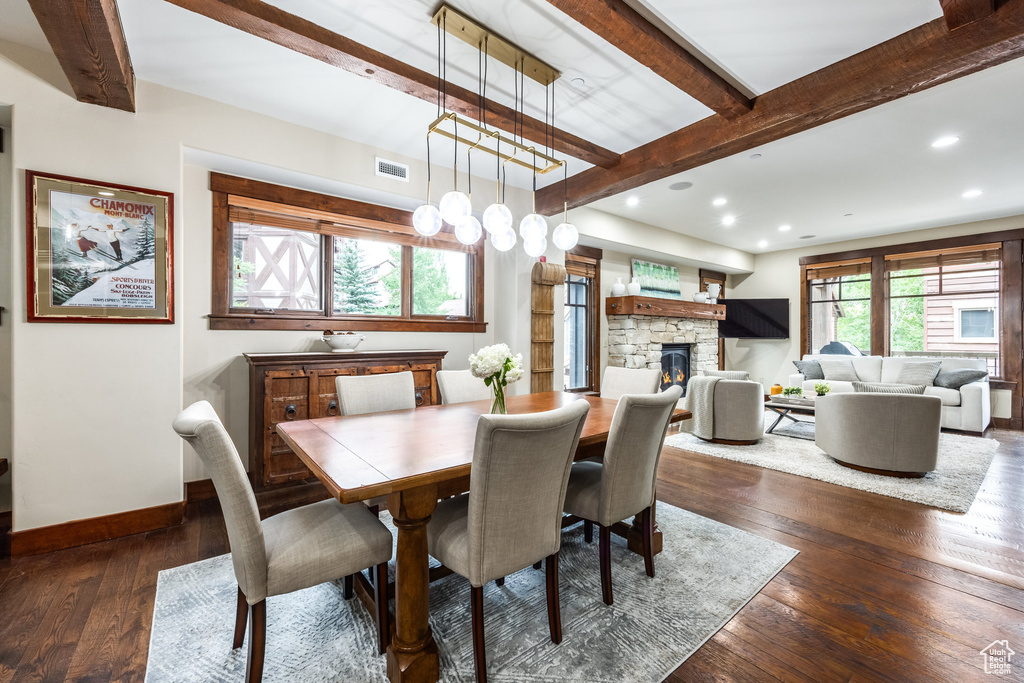Dining room featuring beamed ceiling, dark wood-style floors, a stone fireplace, recessed lighting, and a chandelier