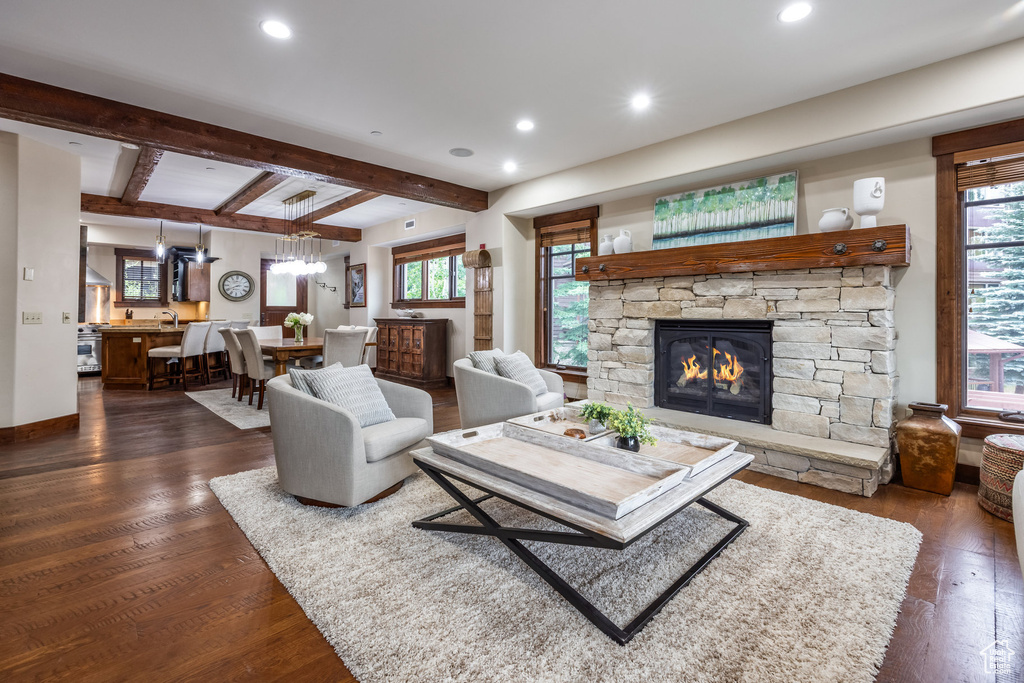 Living room featuring dark wood-style floors, a stone fireplace, recessed lighting, beamed ceiling, and healthy amount of natural light