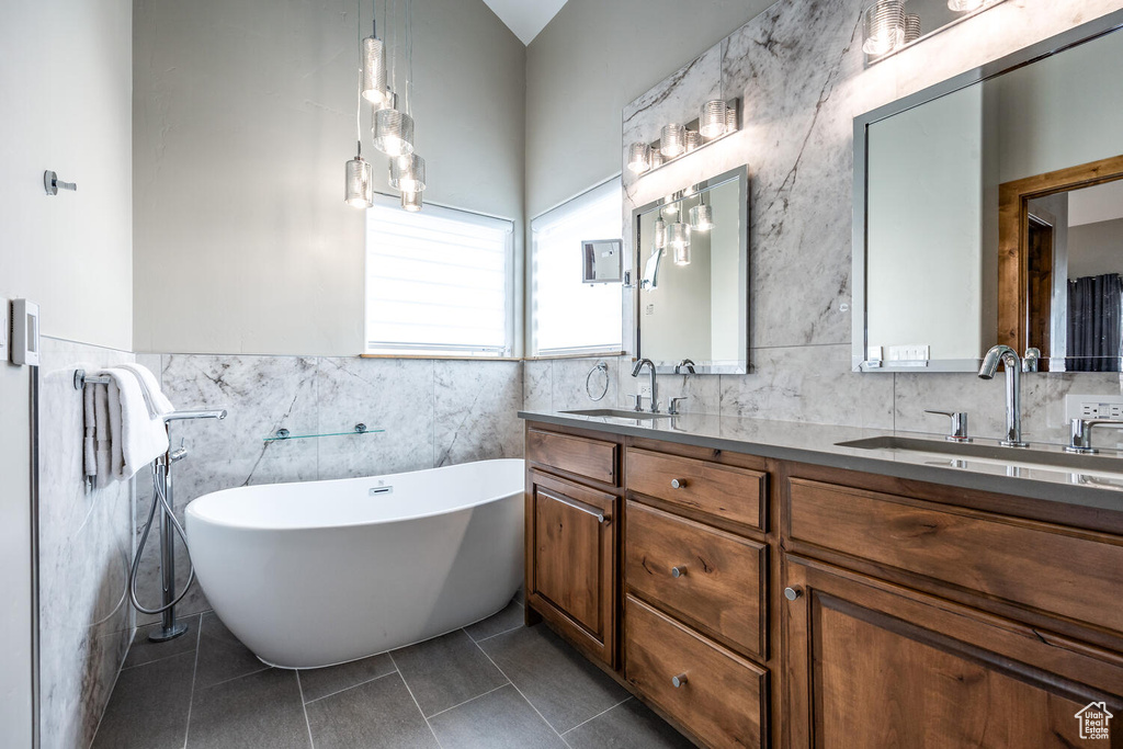 Full bathroom featuring tile walls, double vanity, a freestanding bath, tile patterned floors, and a wainscoted wall