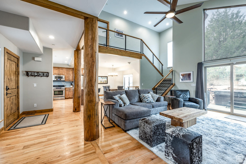 Living area with light wood-style flooring, ceiling fan, a towering ceiling, stairs, and a chandelier