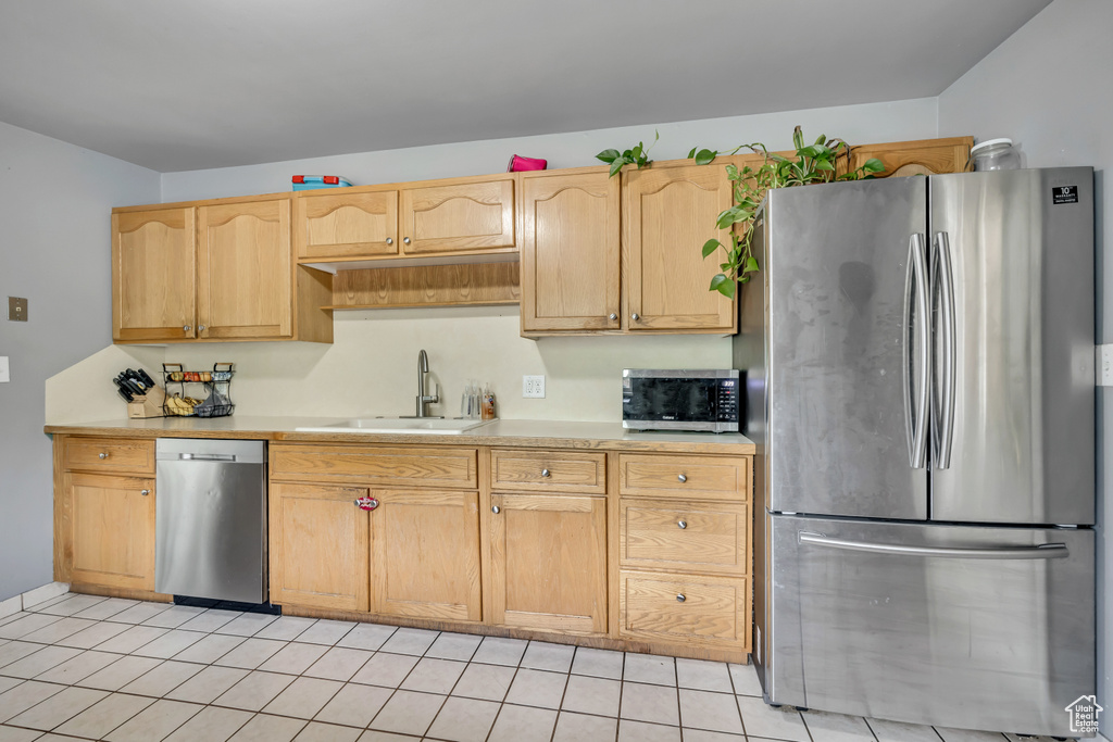 Kitchen with stainless steel appliances, light countertops, light brown cabinetry, and light tile patterned floors