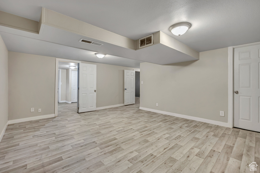 Finished below grade area featuring light wood finished floors and a textured ceiling