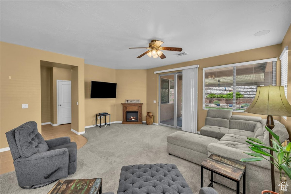 Living room with a ceiling fan, a warm lit fireplace, and carpet flooring