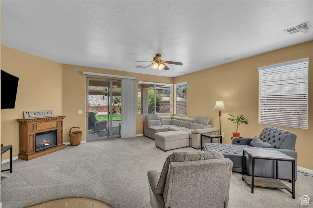 Living room featuring light carpet, a ceiling fan, and a glass covered fireplace