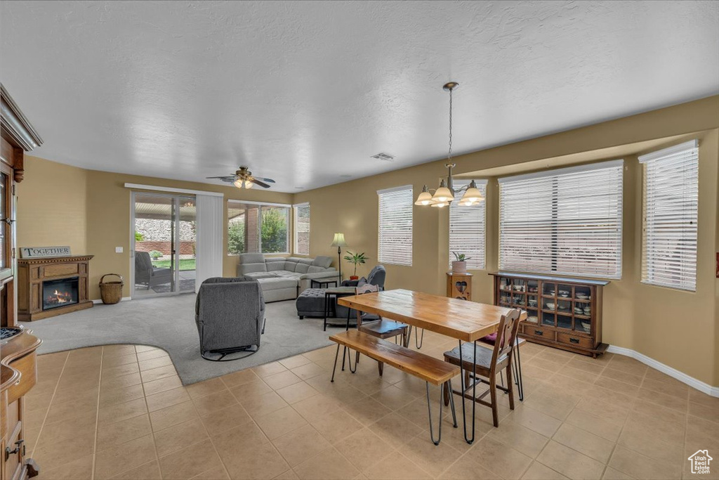 Dining space featuring a chandelier, a glass covered fireplace, light tile patterned flooring, ceiling fan, and a textured ceiling