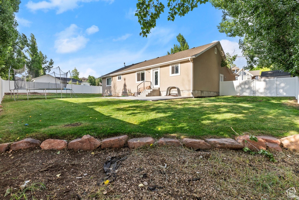 Rear view of property featuring a trampoline, a fenced backyard, stucco siding, and a patio area