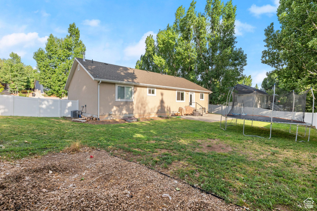 Back of property featuring a trampoline, a fenced backyard, stucco siding, and a shingled roof