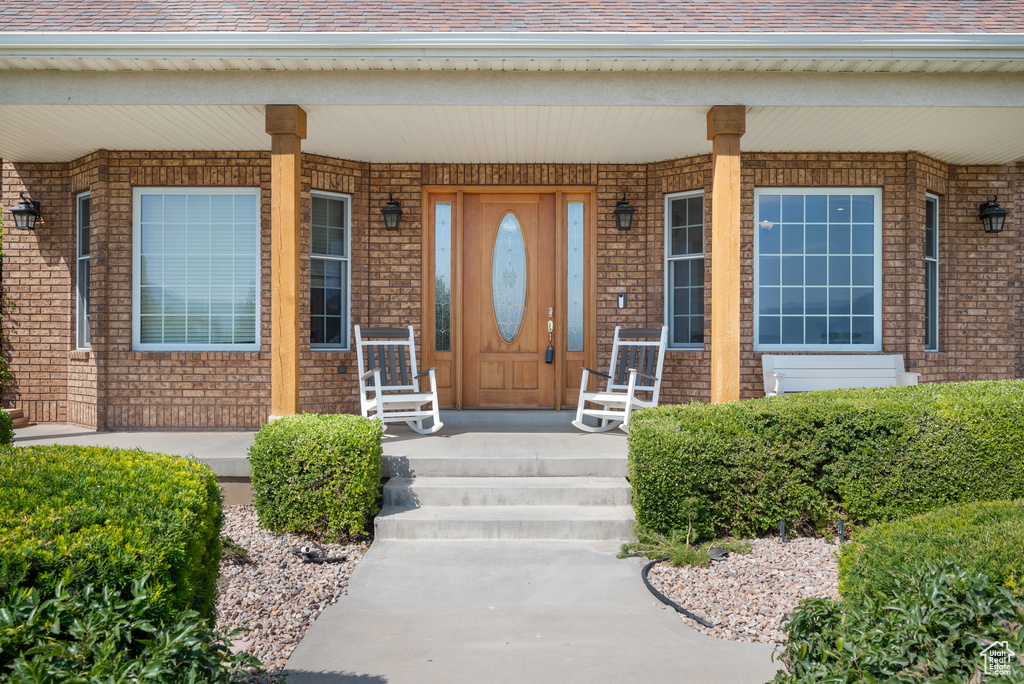 Entrance to property featuring covered porch, brick siding, and roof with shingles