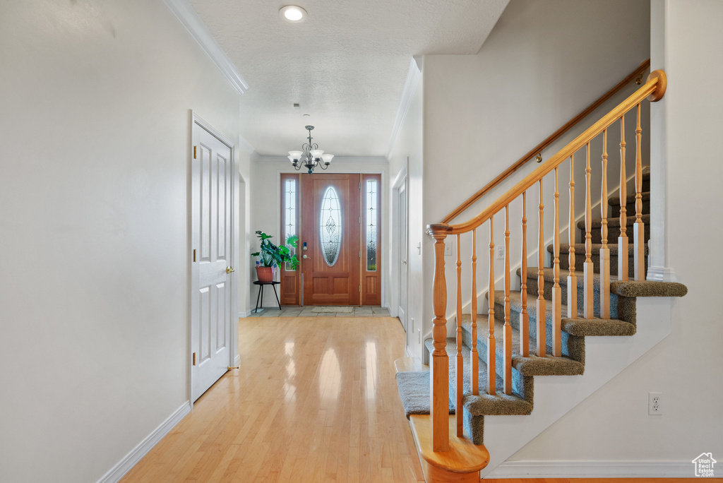 Foyer entrance with a chandelier, wood finished floors, ornamental molding, and stairway