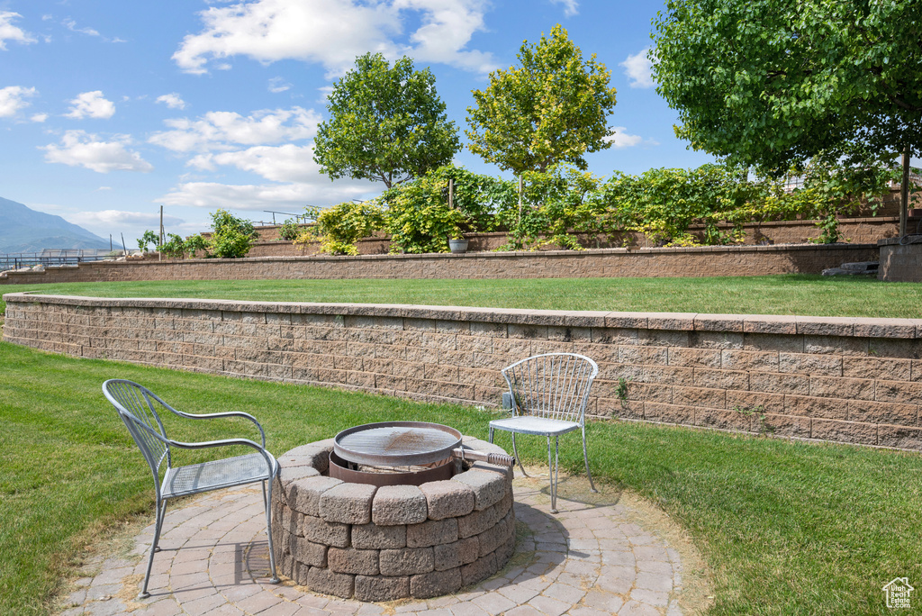 View of green lawn featuring a fire pit, a mountain view, and a patio