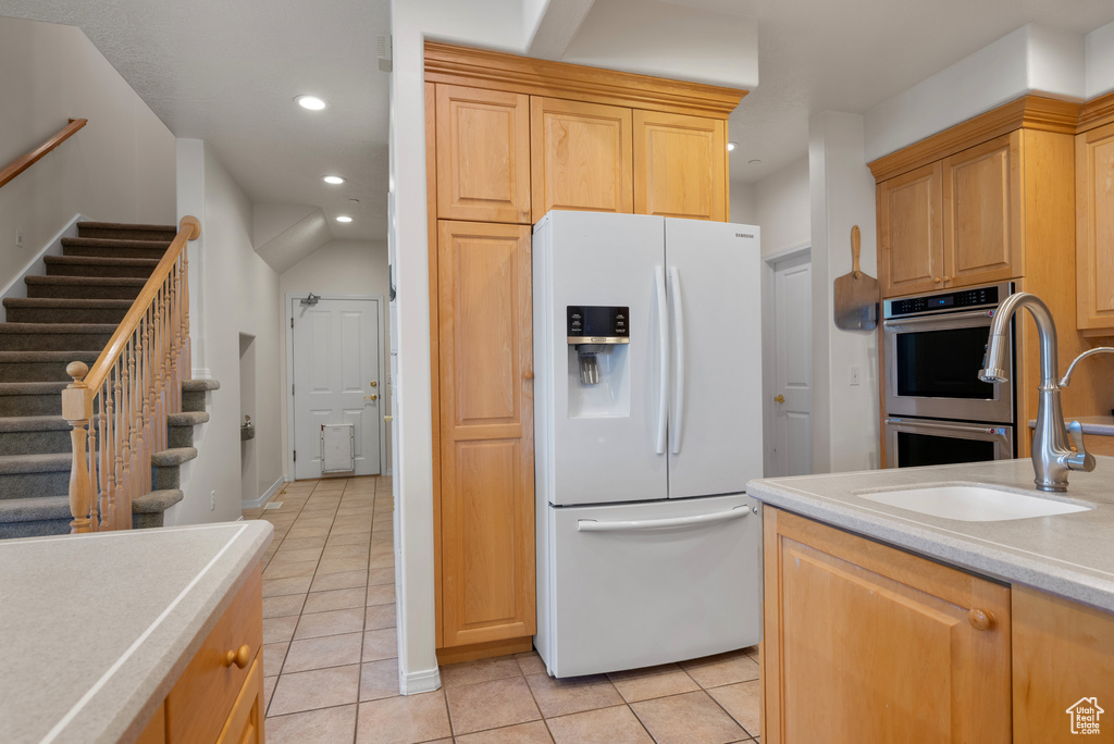 Kitchen featuring white fridge with ice dispenser, double oven, light tile patterned floors, light countertops, and recessed lighting