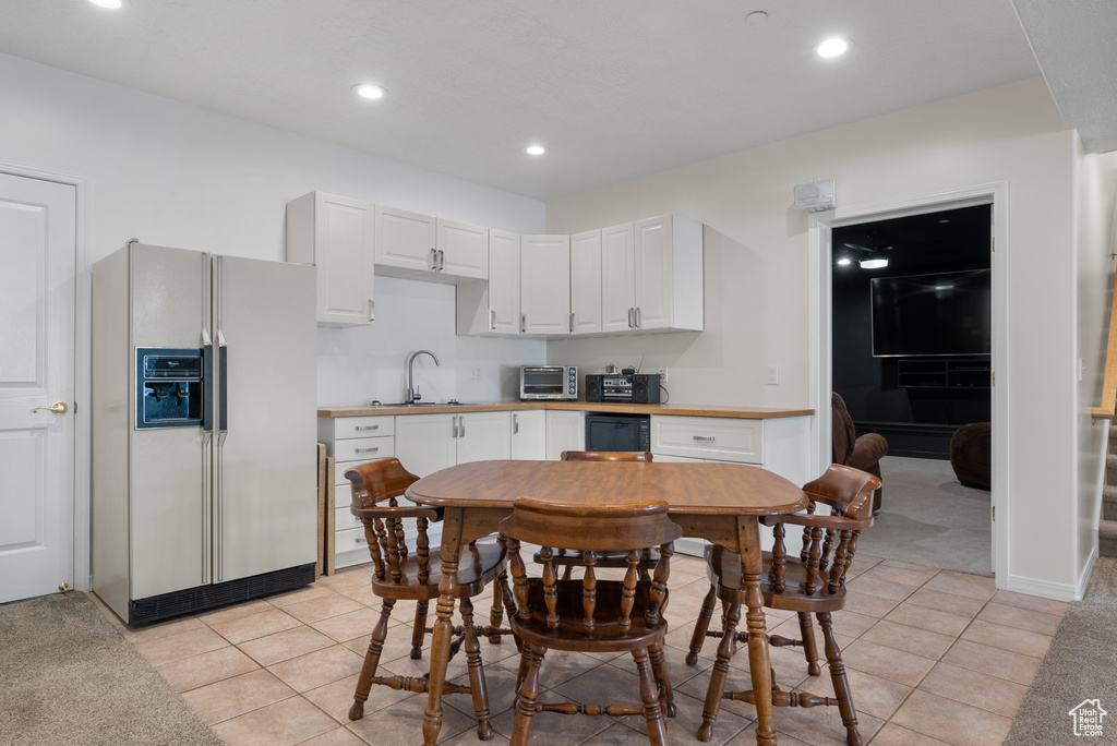 Kitchen featuring white refrigerator with ice dispenser, white cabinetry, recessed lighting, light tile patterned flooring, and light countertops