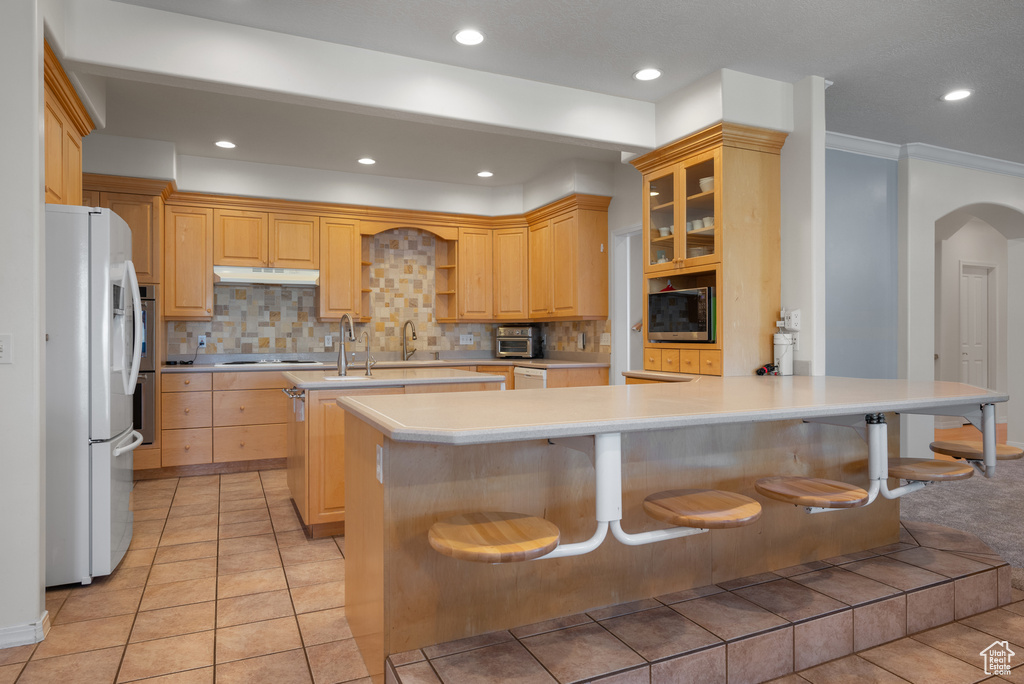 Kitchen featuring freestanding refrigerator, under cabinet range hood, a peninsula, light countertops, and stainless steel microwave