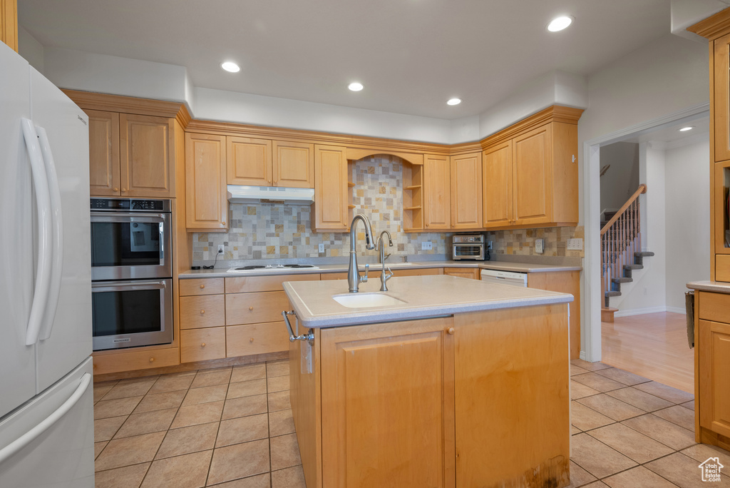 Kitchen featuring white appliances, light countertops, light tile patterned flooring, decorative backsplash, and an island with sink