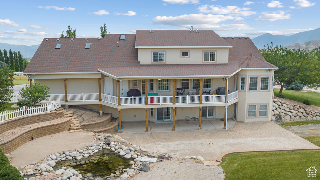 Rear view of house with stucco siding, a patio area, roof with shingles, and a deck with mountain view