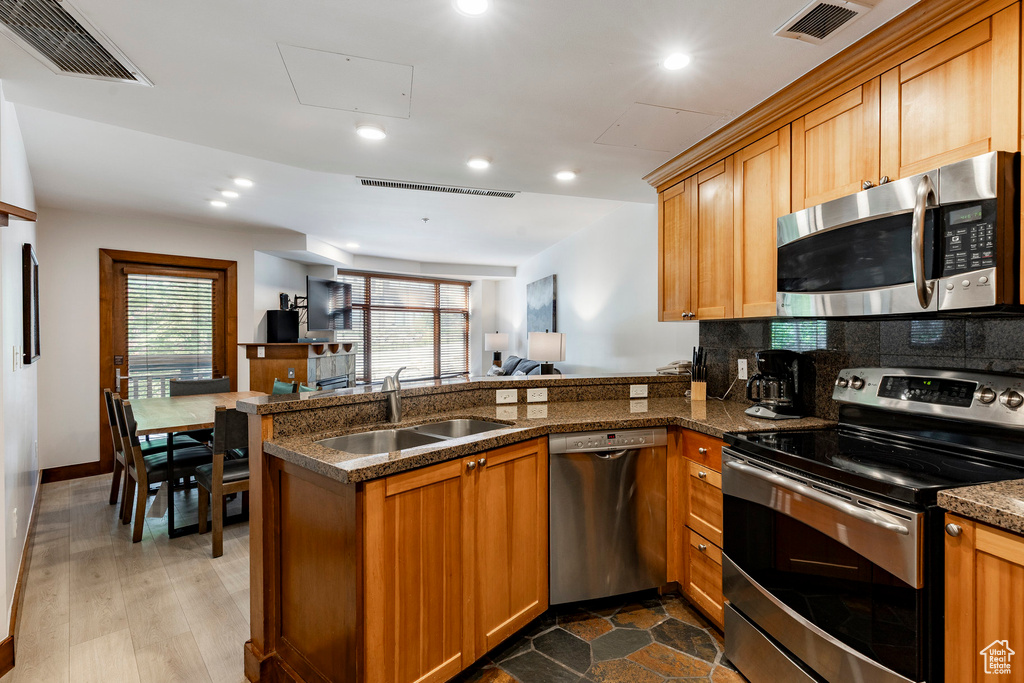 Kitchen featuring appliances with stainless steel finishes, a peninsula, recessed lighting, brown cabinetry, and open floor plan