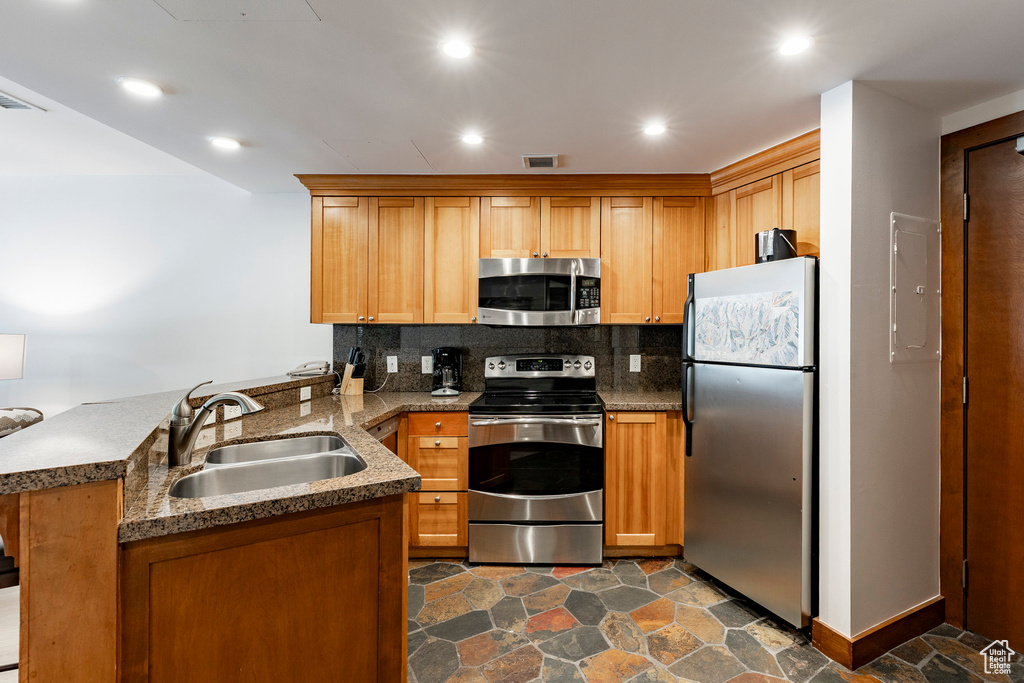 Kitchen featuring appliances with stainless steel finishes, a peninsula, tasteful backsplash, stone countertops, and recessed lighting