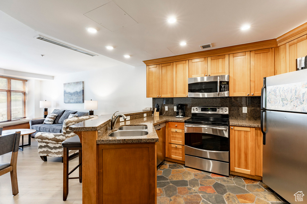 Kitchen with stainless steel appliances, a peninsula, tasteful backsplash, a kitchen bar, and open floor plan