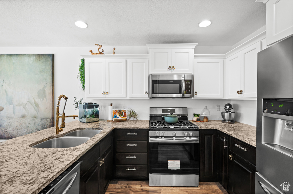 Kitchen featuring stainless steel appliances, white cabinets, dark cabinets, wood finished floors, and light stone countertops